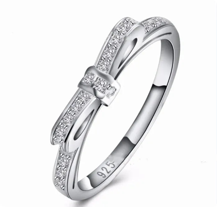 Silver couple ring with bow shape and rhinestone zircon crystals on finger.