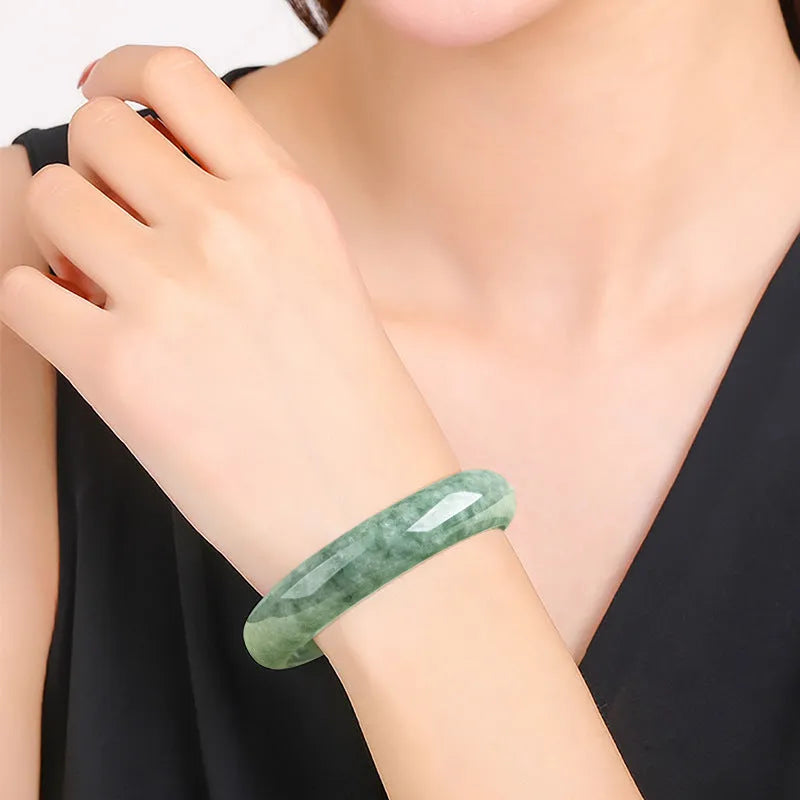 Dark pea green jade bracelet on a wrist, showing its simple band style and natural colour.