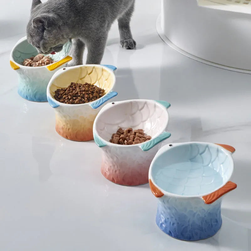 Blue fish-shaped ceramic cat bowl with tilted angle and elevated base on a table.
