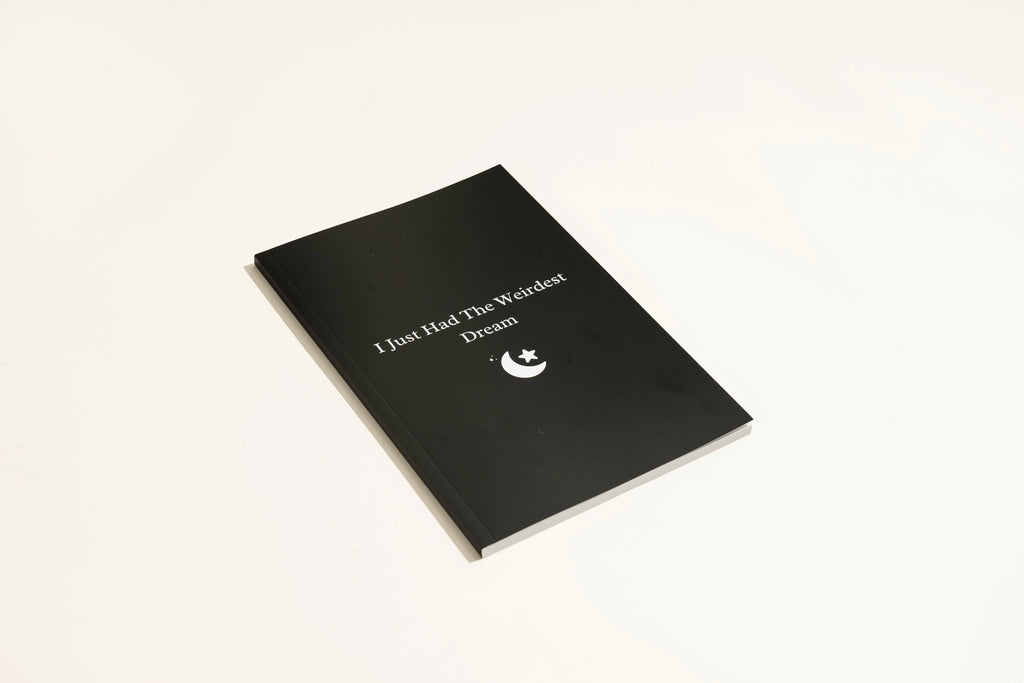 Black cover dream journal notebook with ruled pages open on a desk.