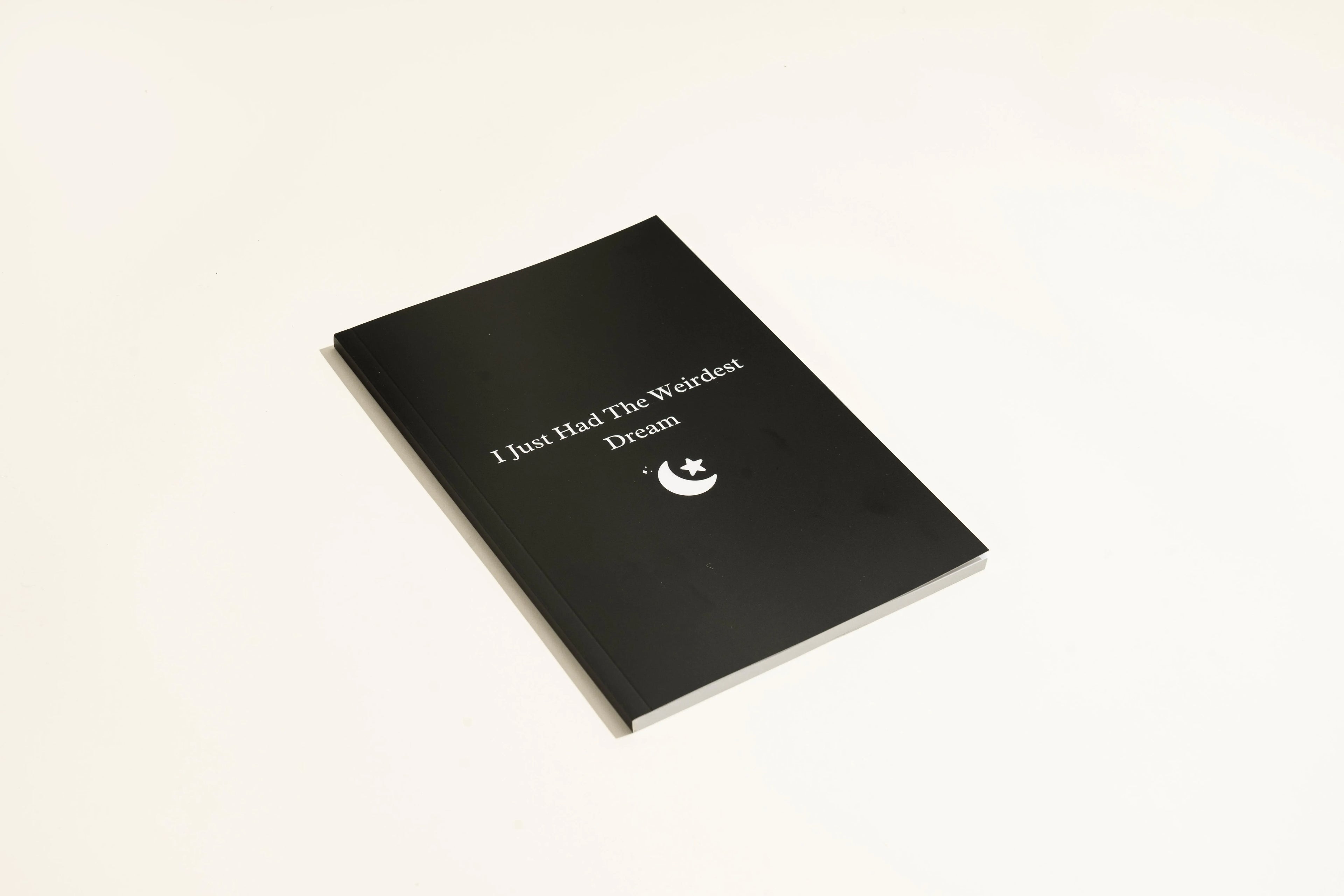Black cover dream journal notebook with ruled pages open on a desk.