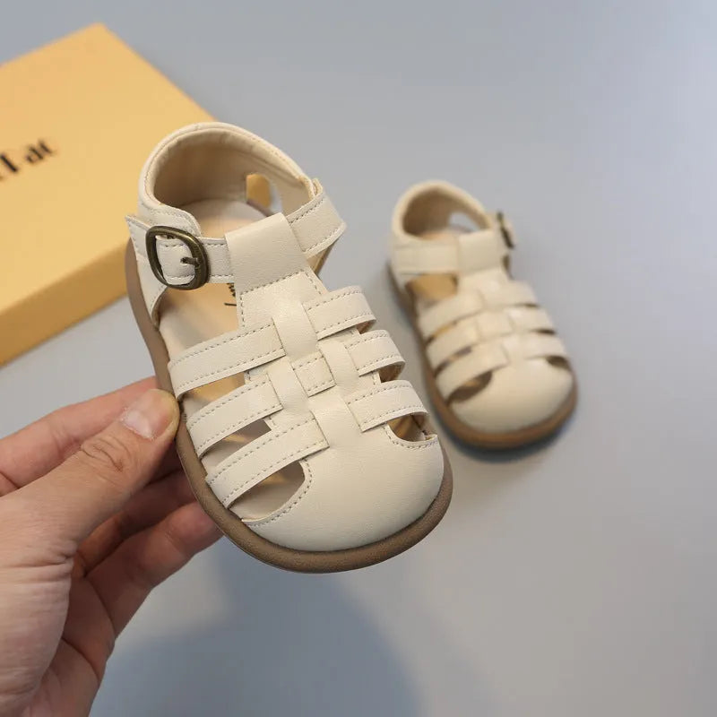 Girls' closed toe PU leather woven hollowed Roman sandals with Velcro strap, beige colour, on toddler feet