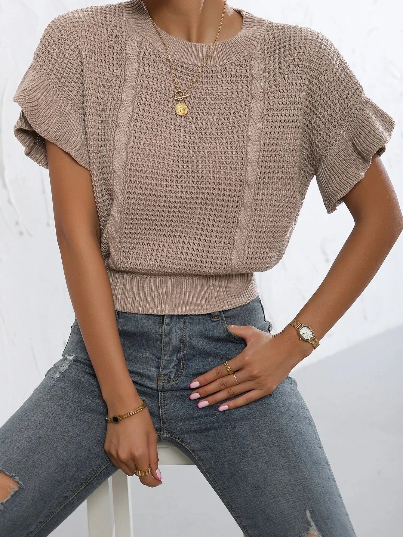 Loose fit knitted pullover sweater with twisted string pattern and ruffled short sleeves on a hanger.