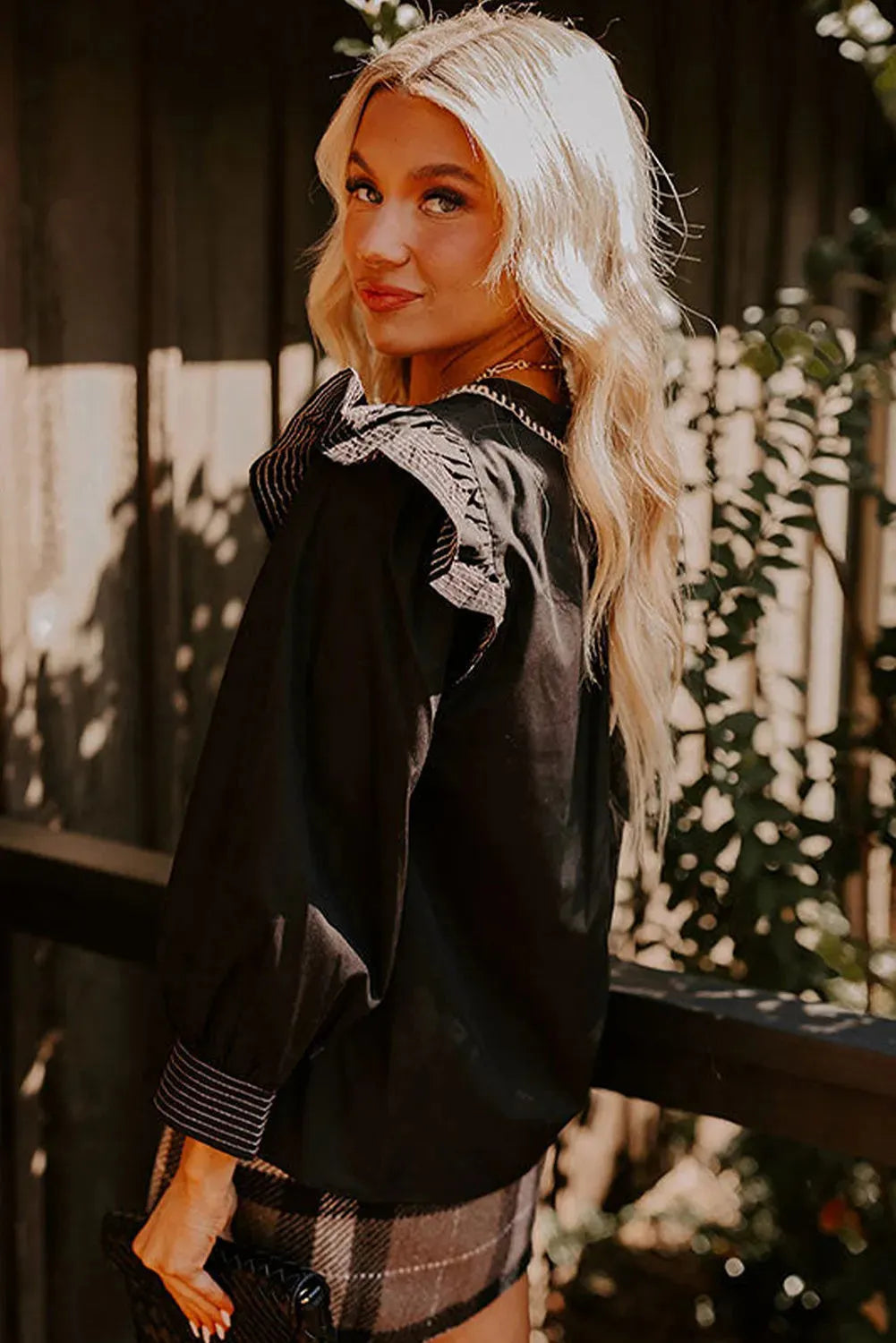 Black women's V-neck blouse with contrast stitching and ruffled long sleeves.