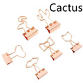 Small gold metal office clip with a long tail handle, shown in decorative bow, cactus, cat, flamingo, and love shapes.