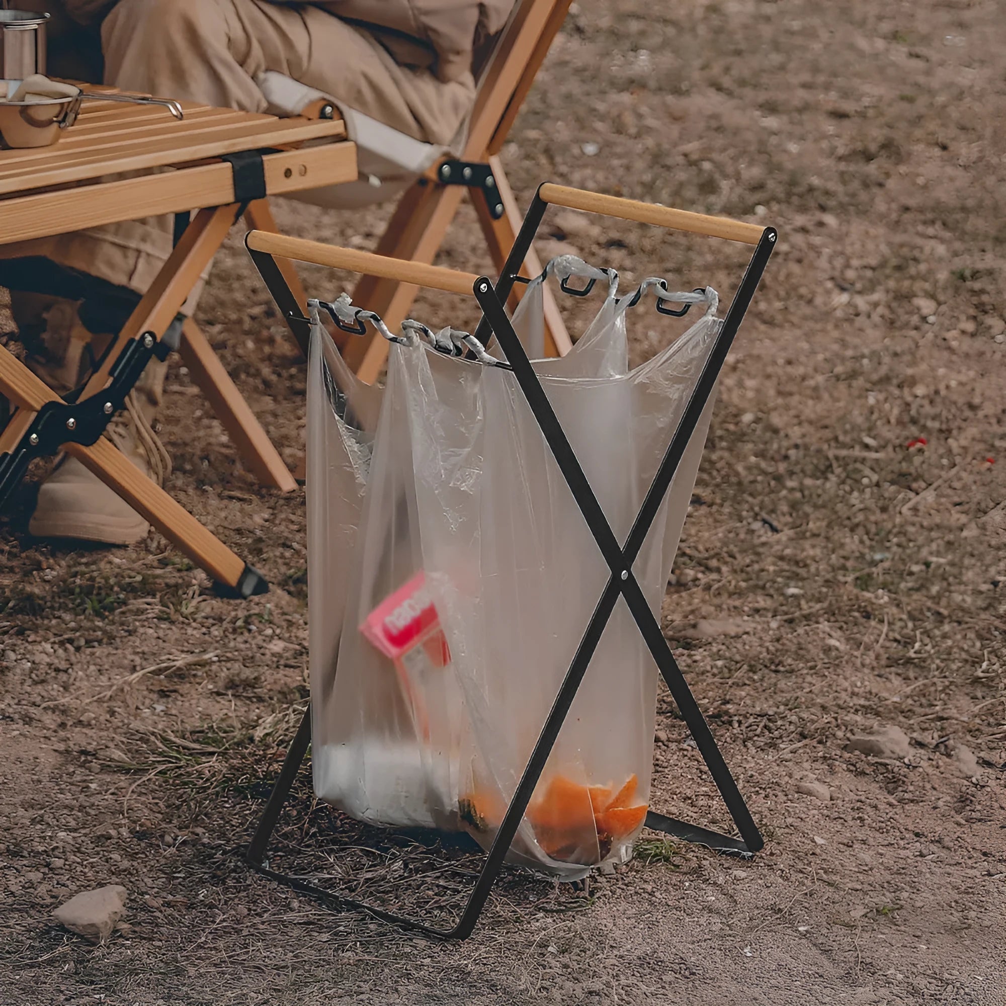 Black outdoor folding trash rack with wooden handle holding a white bin bag open.