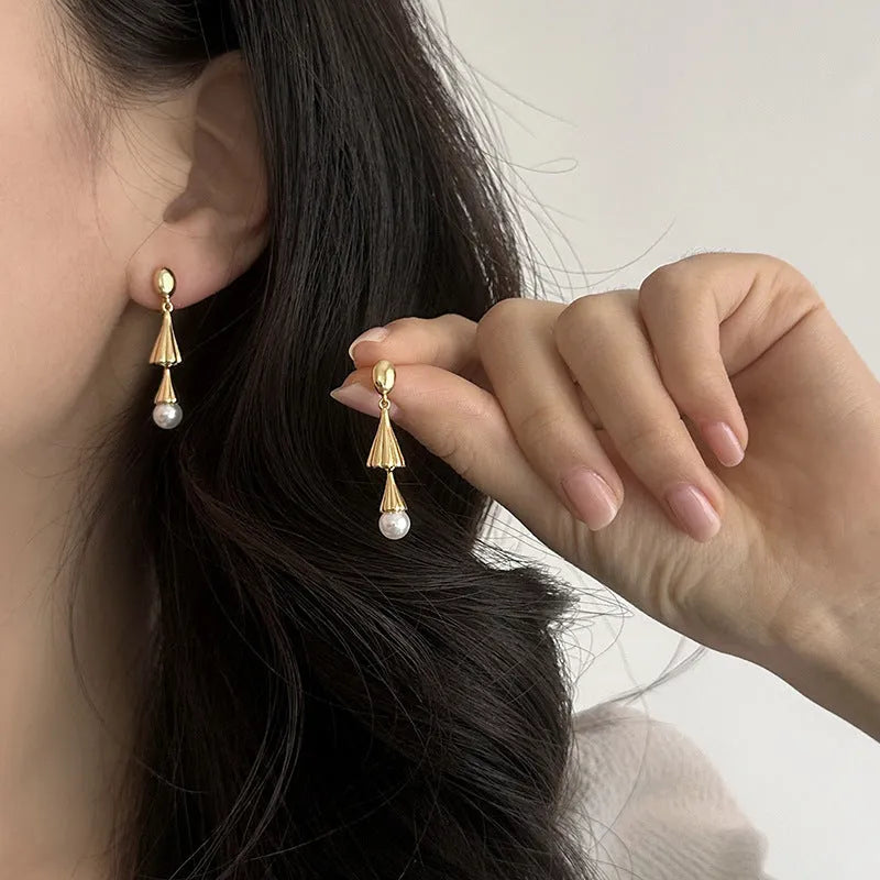Gold electroplated copper geometric fringe earrings on a woman with long wind chime pearl mosquito coil plate shape close up