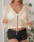 Short apricot coloured women's cardigan blouse with long bell sleeves on a hanger.