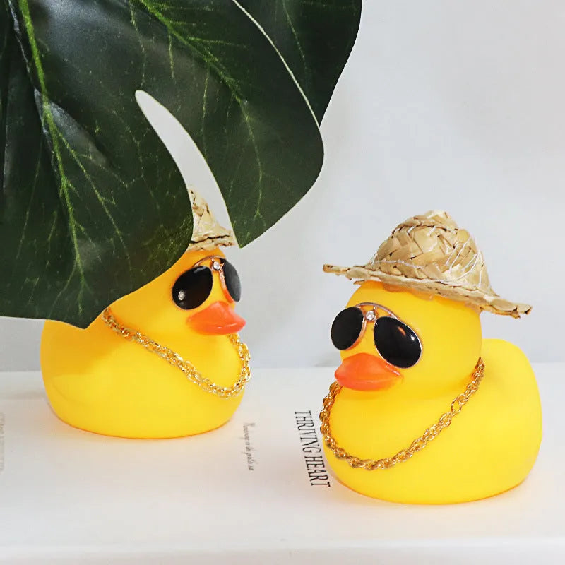 Yellow cartoon duck car ornament wearing a straw hat, with miniature sunglasses accessory.