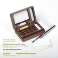 Mini walnut wood watercolour paint box open to show paint pans, with Holbein and Schminke pigment suit options.