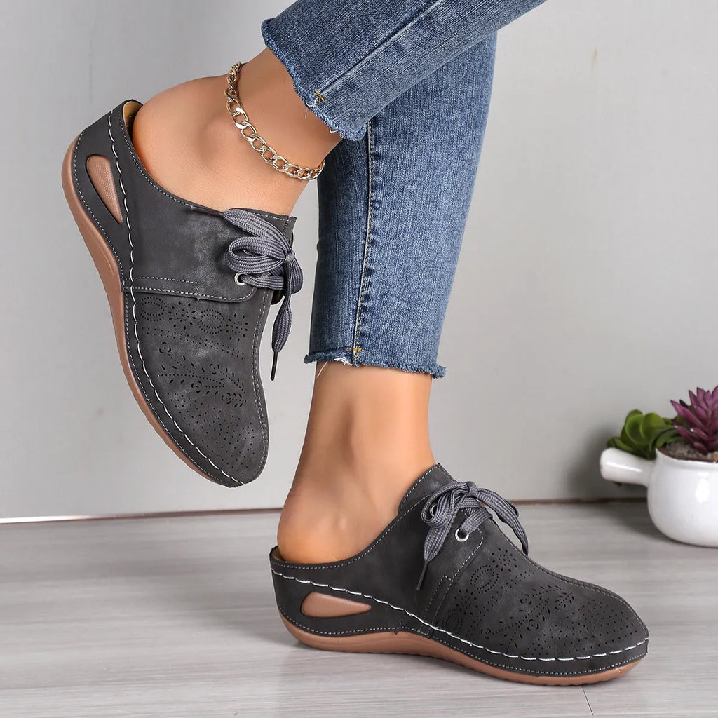 Women's lace-up suede wedge slippers with a hollow-out design, shown in a light colour on a foot.
