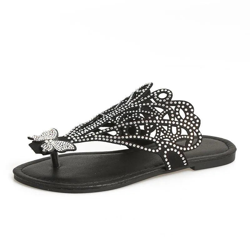 Women's black slip-on sandals with rhinestone decoration on the flip-toe, showing the flat heel and rubber sole.