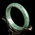 Dark pea green jade bracelet on a wrist, showing its simple band style and natural colour.