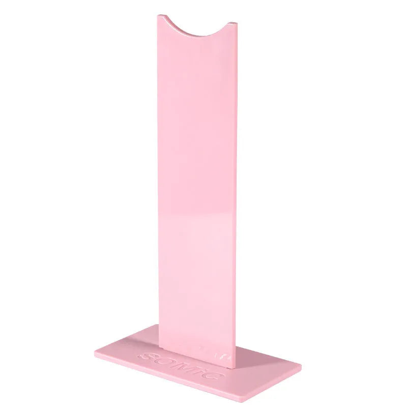 Pink and black foldable head-mounted headset stand with a non-slip silicone base on a desk.