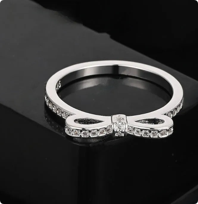Silver couple ring with bow shape and rhinestone zircon crystals on finger.