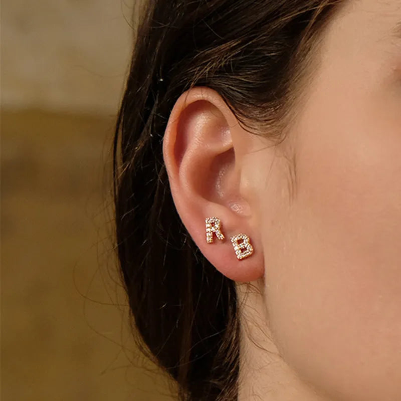 A pair of brass stud earrings featuring a single gold-plated English alphabet letter.