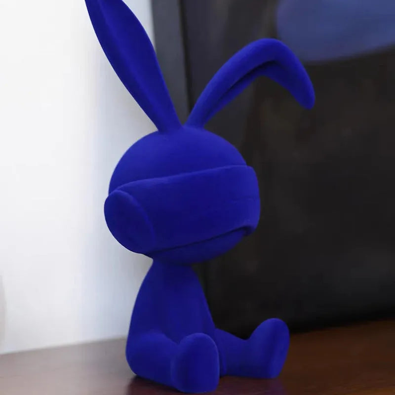 Small blue resin ornament of a rabbit wearing a blindfold on a wooden table.
