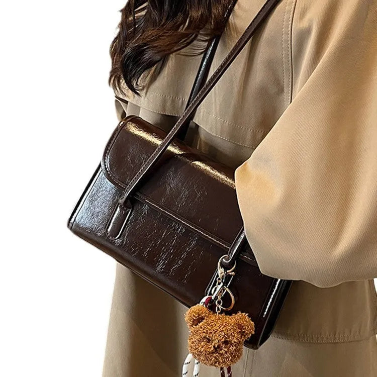 Brown women's square shoulder bag with pendant detail and adjustable crossbody straps on table