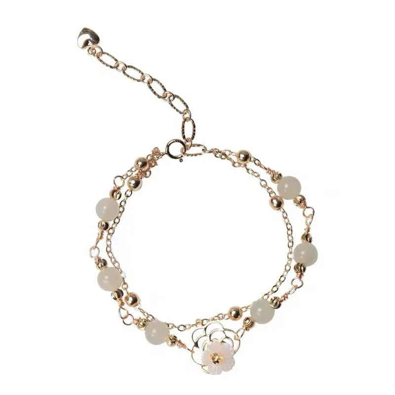 Yellow gold electroplated women's bracelet with butterfly and shell flower charms on a chain.