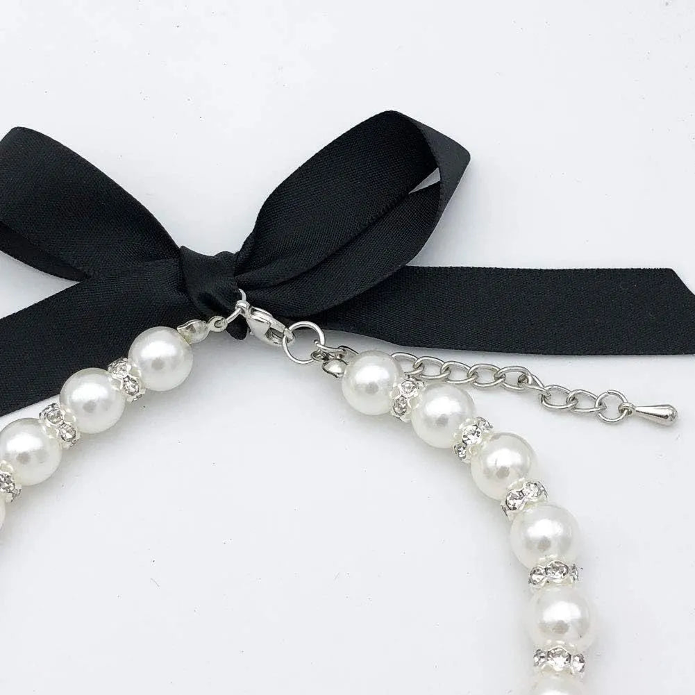 Small dog wearing a blue adjustable pearl and rhinestone necklace collar with a ribbon bow.