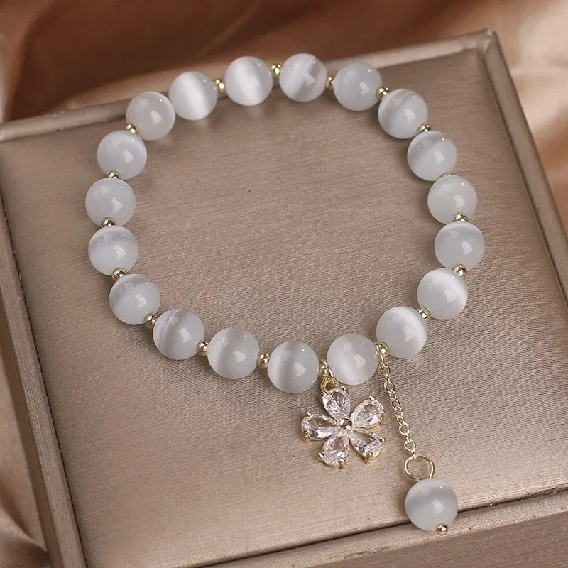 Single loop women's bracelet with white cat's eye stone, small flower tassel, and morganite safety buckle pendant.