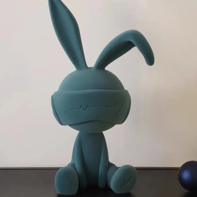 Small blue resin ornament of a rabbit wearing a blindfold on a wooden table.
