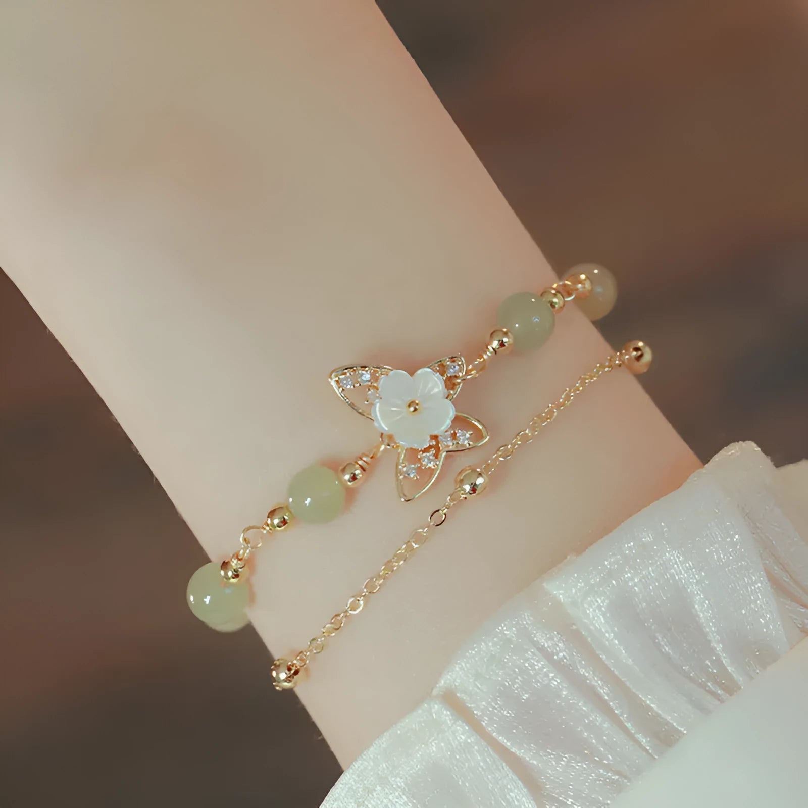Yellow gold electroplated women's bracelet with butterfly and shell flower charms on a chain.