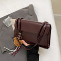 Brown women's square shoulder bag with pendant detail and adjustable crossbody straps on table