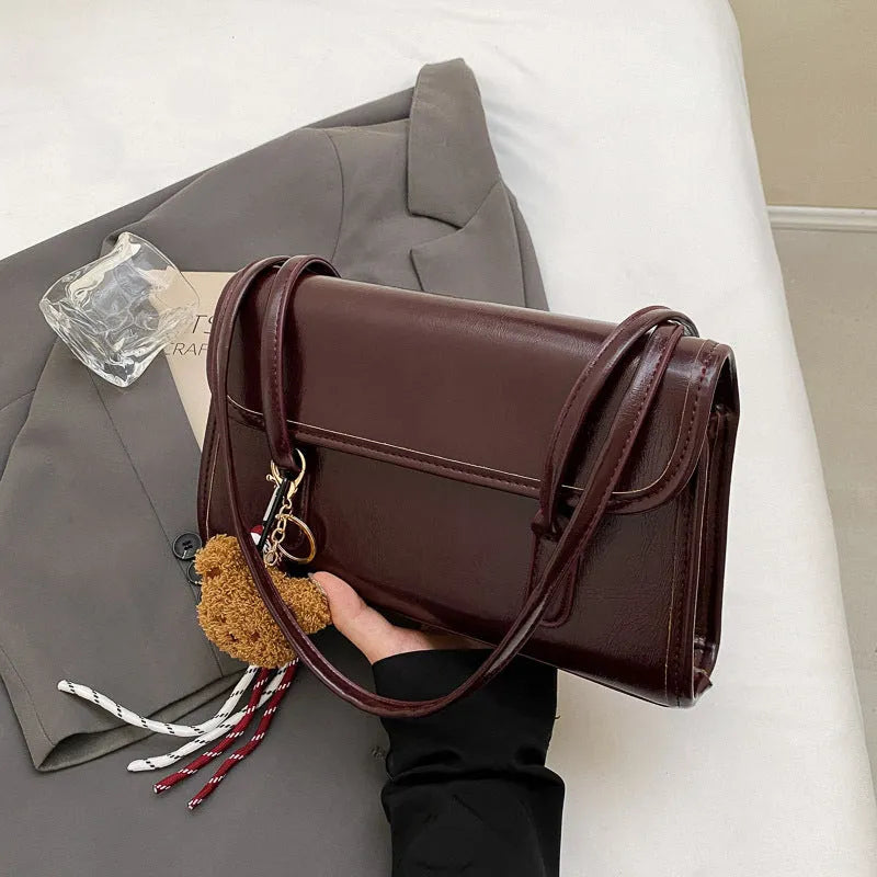 Brown women's square shoulder bag with pendant detail and adjustable crossbody straps on table