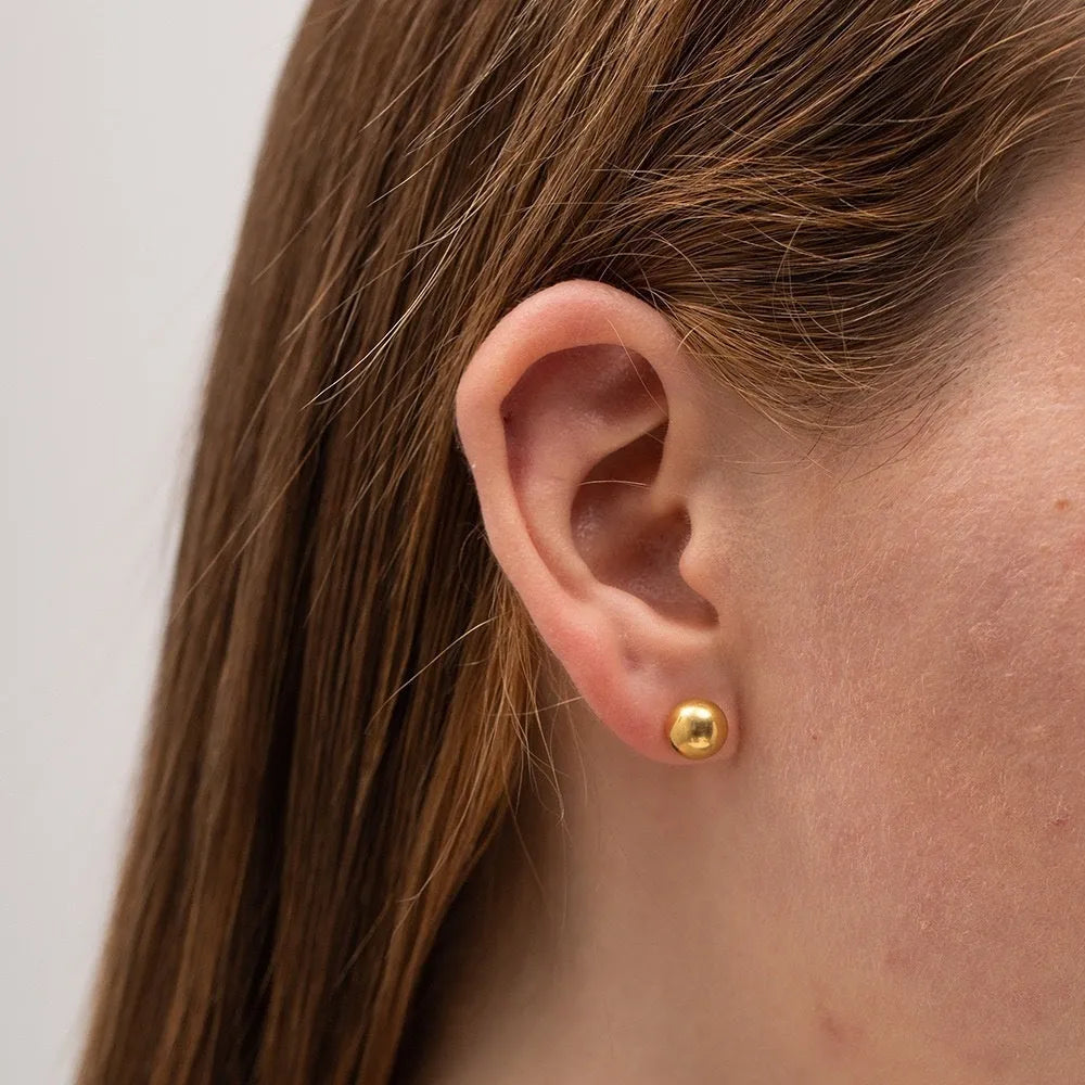 Minimalist round ball stud earrings in gold and silver tones on a plain background.