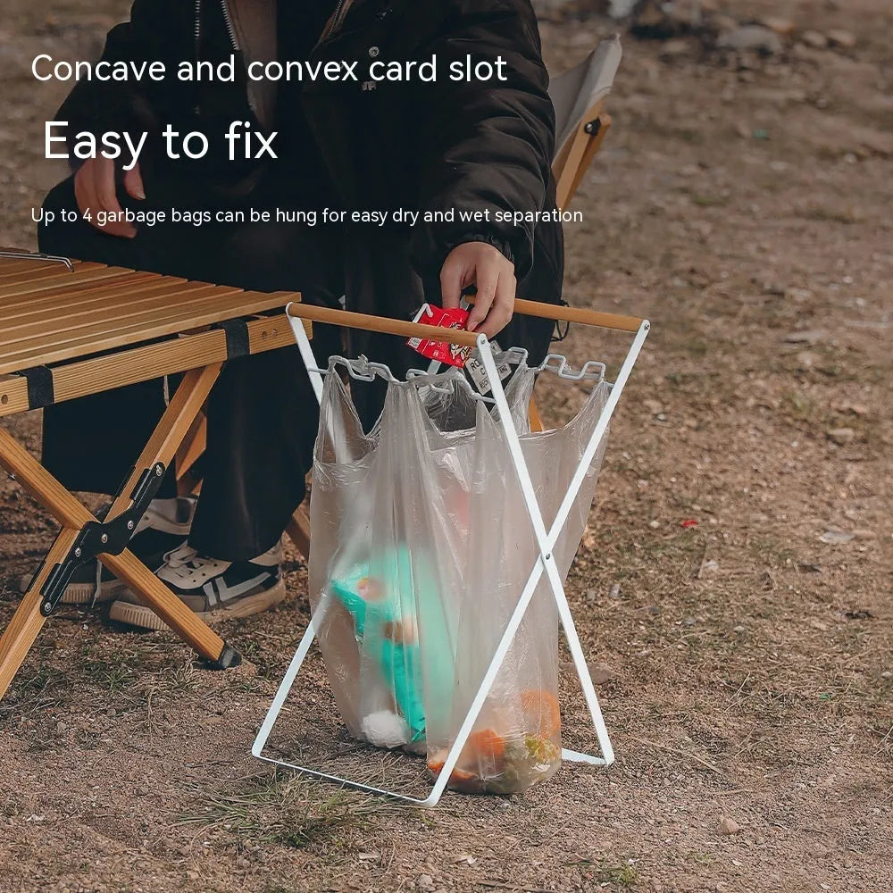 Black outdoor folding trash rack with wooden handle holding a white bin bag open.